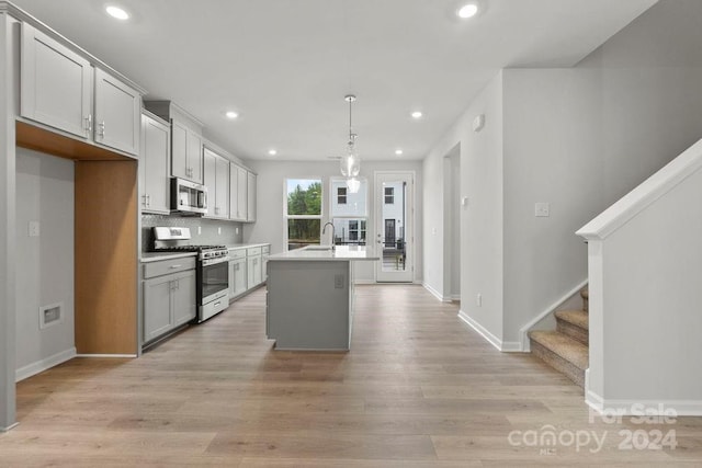 kitchen with pendant lighting, sink, a center island with sink, stainless steel appliances, and light wood-type flooring