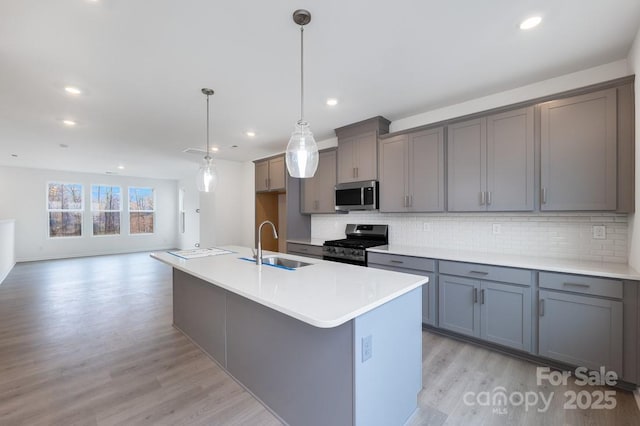 kitchen featuring hanging light fixtures, gray cabinetry, stainless steel appliances, an island with sink, and sink