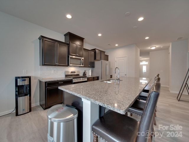 kitchen featuring light stone counters, a breakfast bar, stainless steel appliances, light hardwood / wood-style flooring, and sink