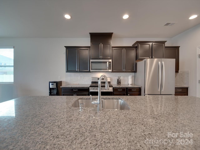 kitchen with light stone countertops, stainless steel appliances, dark brown cabinetry, and sink