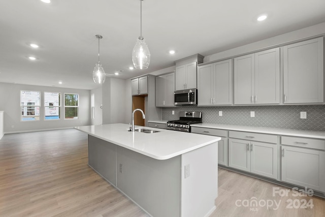 kitchen with gray cabinets, light wood-type flooring, sink, an island with sink, and appliances with stainless steel finishes