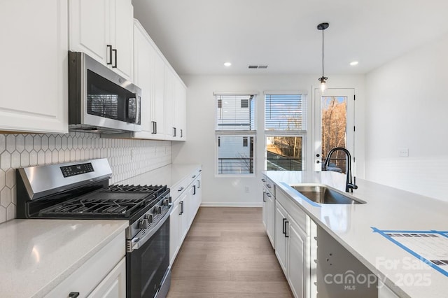 kitchen with sink, stainless steel appliances, white cabinets, hanging light fixtures, and tasteful backsplash