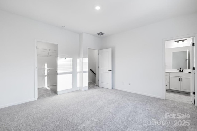 unfurnished bedroom with sink, ensuite bath, light colored carpet, and a spacious closet