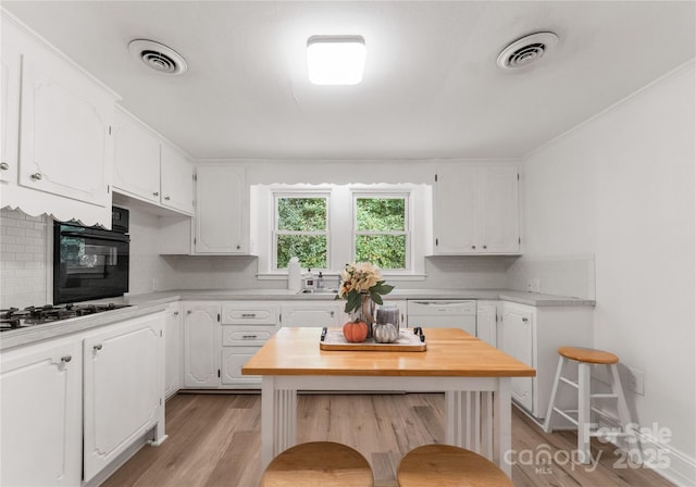 kitchen featuring light wood-type flooring, gas cooktop, dishwasher, white cabinets, and backsplash