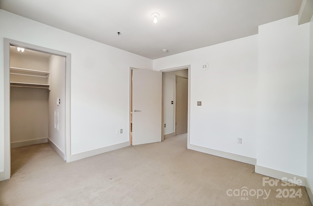 unfurnished bedroom with light colored carpet, a closet, and a spacious closet