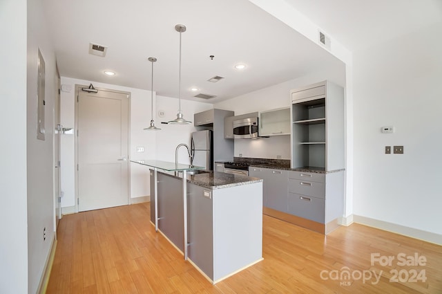 kitchen featuring hanging light fixtures, gray cabinetry, a center island with sink, light hardwood / wood-style flooring, and stainless steel appliances