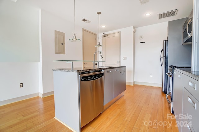 kitchen with light wood-type flooring, electric panel, sink, hanging light fixtures, and stainless steel appliances