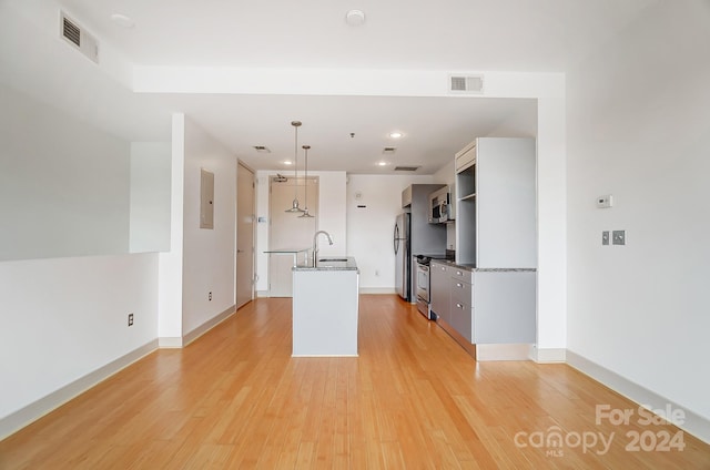 kitchen with light wood-type flooring, sink, an island with sink, hanging light fixtures, and appliances with stainless steel finishes