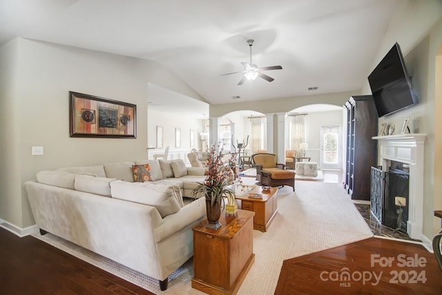 living area featuring vaulted ceiling, wood finished floors, arched walkways, decorative columns, and ceiling fan
