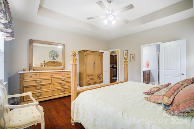 bedroom with ceiling fan, connected bathroom, a raised ceiling, and dark wood finished floors