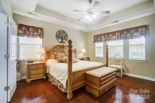 bedroom featuring baseboards, visible vents, a raised ceiling, and dark wood finished floors