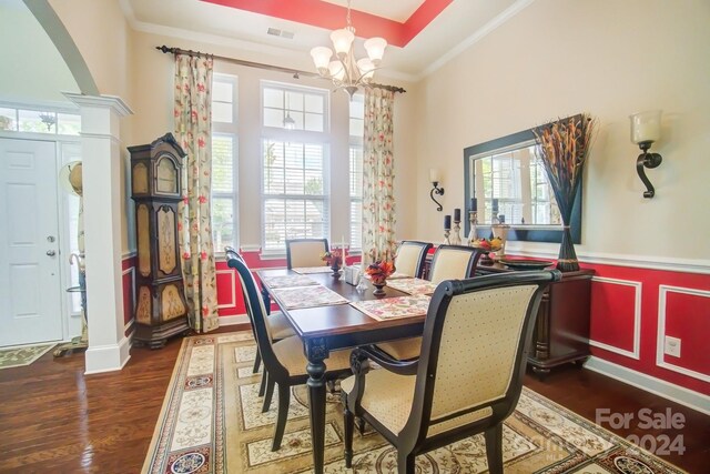 dining space featuring an inviting chandelier, ornamental molding, wood finished floors, and ornate columns