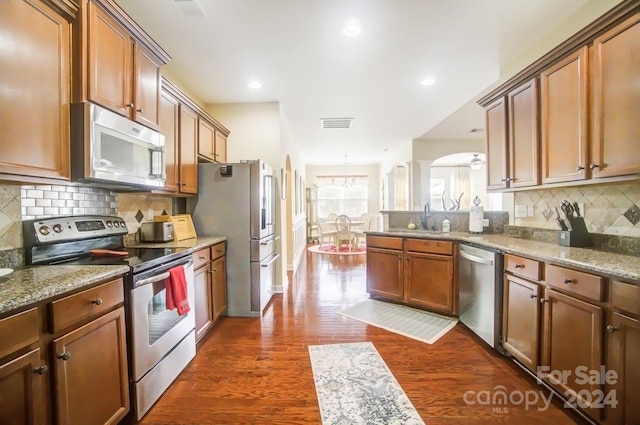 kitchen with dark wood finished floors, arched walkways, light stone countertops, tasteful backsplash, and appliances with stainless steel finishes
