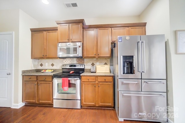 kitchen featuring wood-type flooring, appliances with stainless steel finishes, light stone counters, and decorative backsplash