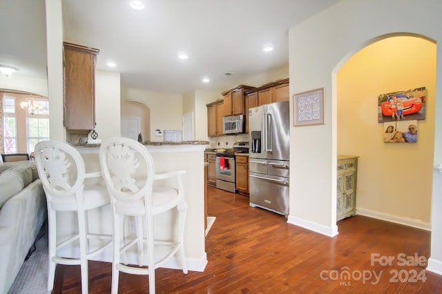 kitchen featuring arched walkways, dark wood-type flooring, a kitchen bar, brown cabinetry, and appliances with stainless steel finishes