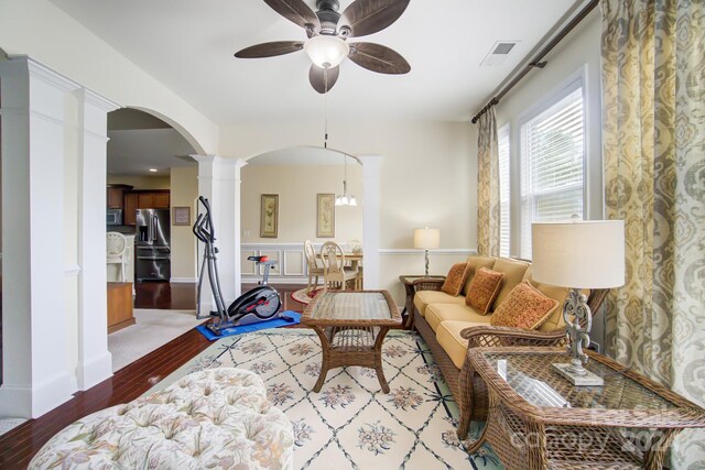 living room featuring wood finished floors, visible vents, a ceiling fan, arched walkways, and decorative columns