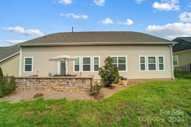 rear view of house featuring a lawn, fence, a patio area, and a shingled roof