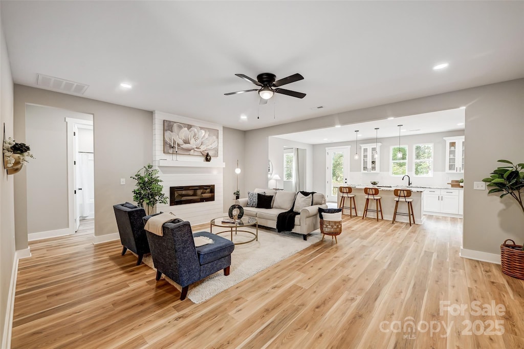 living room featuring a large fireplace, ceiling fan, light hardwood / wood-style floors, and sink