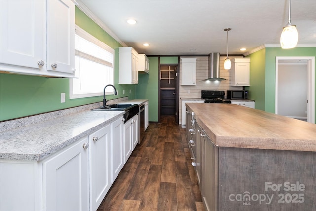 kitchen with sink, black appliances, hanging light fixtures, wall chimney range hood, and white cabinets