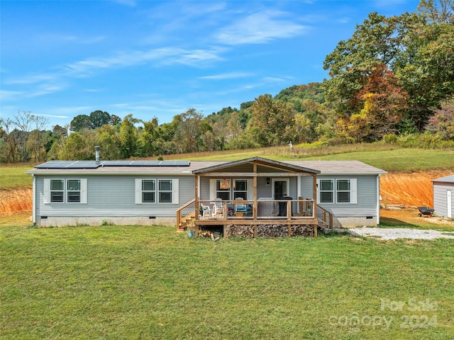 manufactured / mobile home with a wooden deck, a front lawn, and solar panels