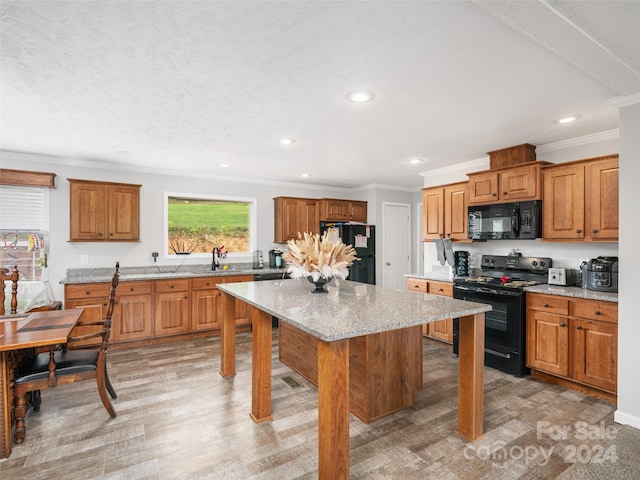 kitchen with black appliances, crown molding, a center island, and light stone counters