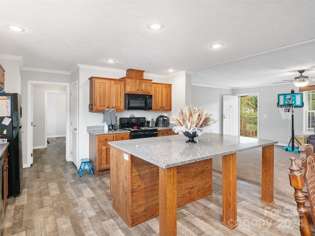 kitchen with light stone counters, a breakfast bar, a kitchen island, black appliances, and ceiling fan