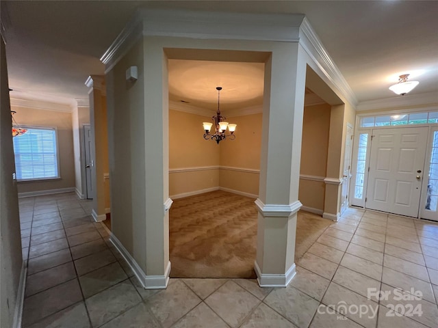 carpeted entryway featuring crown molding, decorative columns, and a chandelier