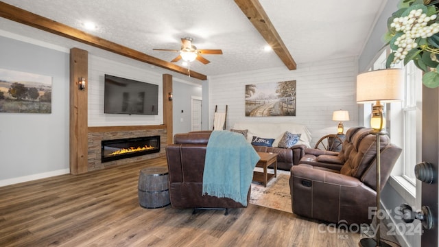 living room featuring ceiling fan, a stone fireplace, beamed ceiling, and dark hardwood / wood-style floors