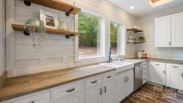 kitchen with wooden walls, stainless steel dishwasher, white cabinetry, and wooden counters