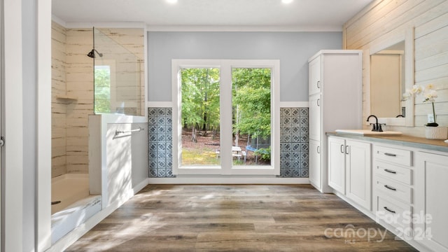 bathroom with tile walls, wood-type flooring, crown molding, tiled shower, and vanity