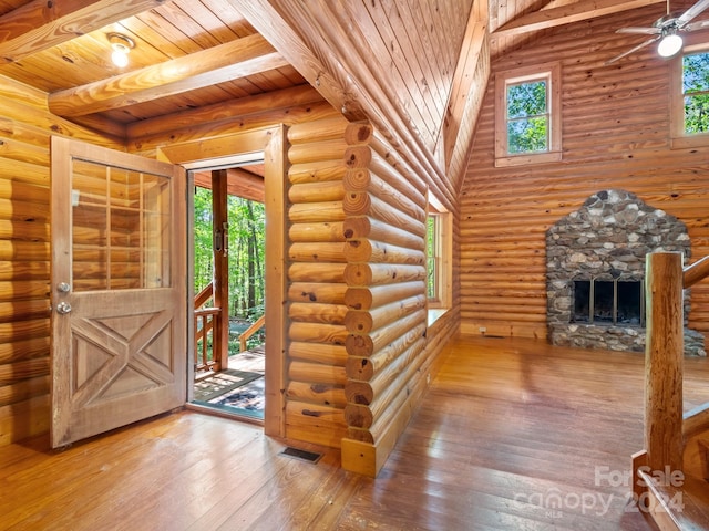 entrance foyer with a stone fireplace, wooden ceiling, wood-type flooring, ceiling fan, and rustic walls