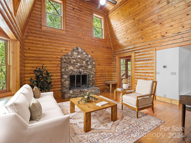 living room featuring wood ceiling, light hardwood / wood-style floors, high vaulted ceiling, a stone fireplace, and ceiling fan