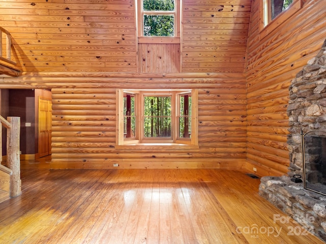 unfurnished living room with a high ceiling, log walls, hardwood / wood-style flooring, and a stone fireplace