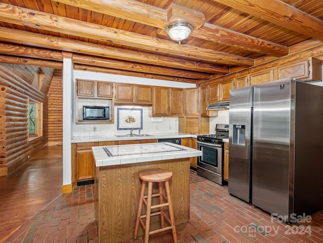 kitchen with stainless steel appliances, a center island, tile counters, sink, and rustic walls