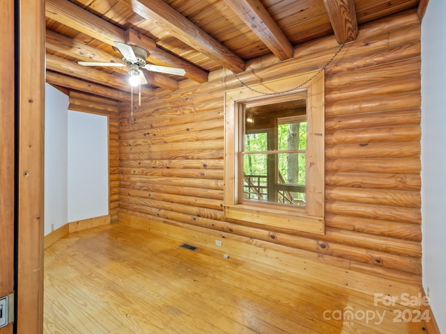 empty room featuring beamed ceiling, wooden ceiling, light wood-type flooring, ceiling fan, and rustic walls