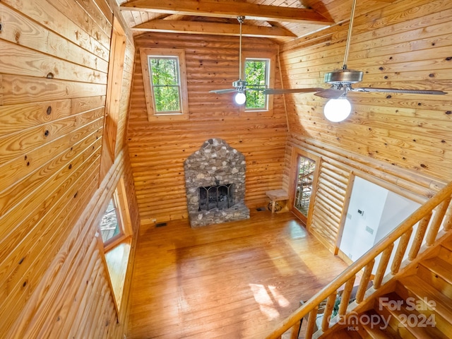 living room with ceiling fan, a stone fireplace, log walls, hardwood / wood-style flooring, and lofted ceiling with beams