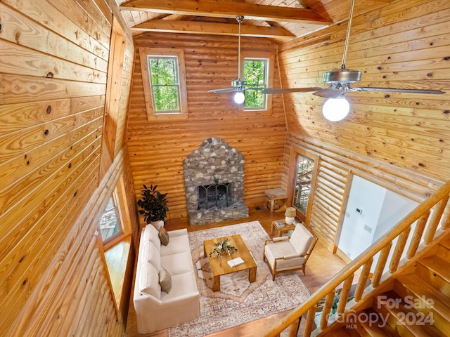 living room with vaulted ceiling with beams, a stone fireplace, hardwood / wood-style floors, and ceiling fan