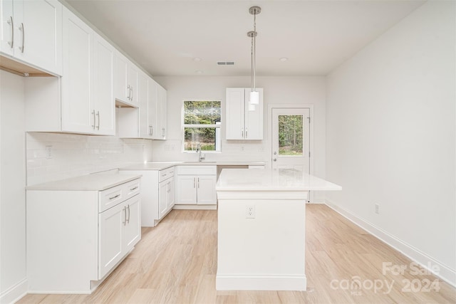 kitchen with white cabinetry, backsplash, hanging light fixtures, light hardwood / wood-style flooring, and a center island