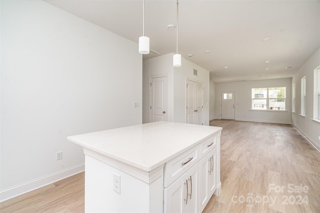 kitchen with light wood-type flooring, white cabinetry, decorative light fixtures, and a kitchen island