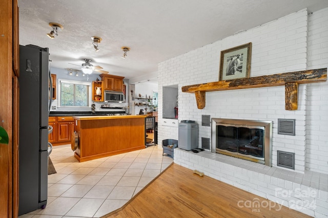 kitchen with a kitchen bar, black refrigerator, kitchen peninsula, light tile patterned floors, and ceiling fan