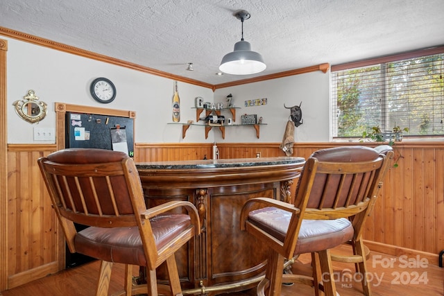 bar featuring wood walls, hardwood / wood-style floors, ornamental molding, and a textured ceiling