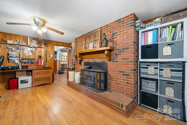 living room with a wood stove, a textured ceiling, wood walls, hardwood / wood-style floors, and ceiling fan