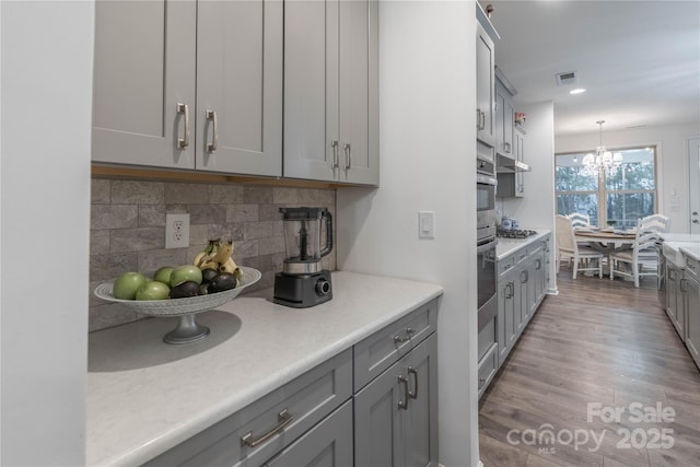 kitchen with light hardwood / wood-style flooring, tasteful backsplash, hanging light fixtures, stainless steel gas cooktop, and gray cabinetry