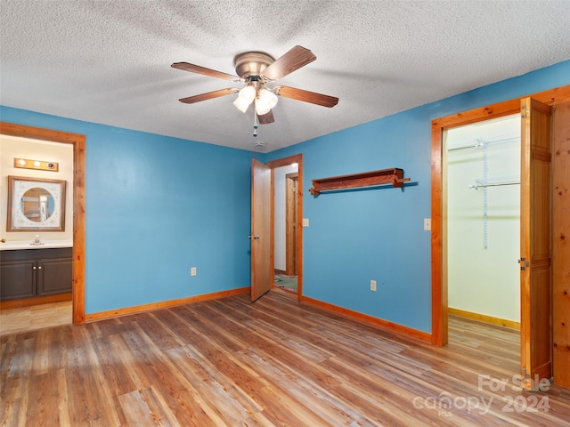 unfurnished bedroom with ceiling fan, connected bathroom, a textured ceiling, hardwood / wood-style flooring, and a closet