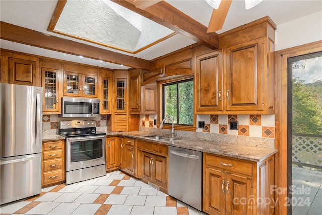 kitchen featuring light stone countertops, backsplash, stainless steel appliances, sink, and beam ceiling