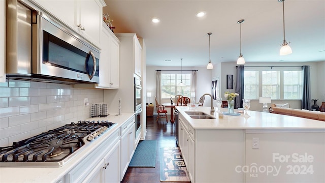 kitchen featuring white cabinetry, sink, stainless steel appliances, decorative light fixtures, and a center island with sink