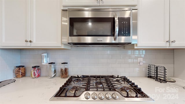 kitchen with appliances with stainless steel finishes, tasteful backsplash, light stone counters, and white cabinetry