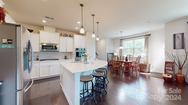 kitchen featuring decorative light fixtures, white cabinetry, an island with sink, and appliances with stainless steel finishes