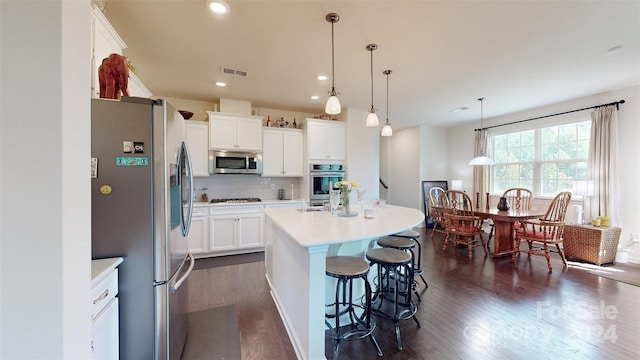 kitchen featuring pendant lighting, a kitchen island with sink, dark hardwood / wood-style flooring, white cabinetry, and stainless steel appliances