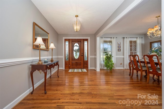 entryway with a textured ceiling, wood-type flooring, and a chandelier